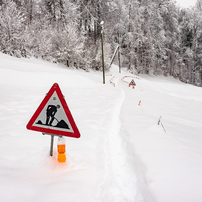 A construction road sign in a winter landscape with trees